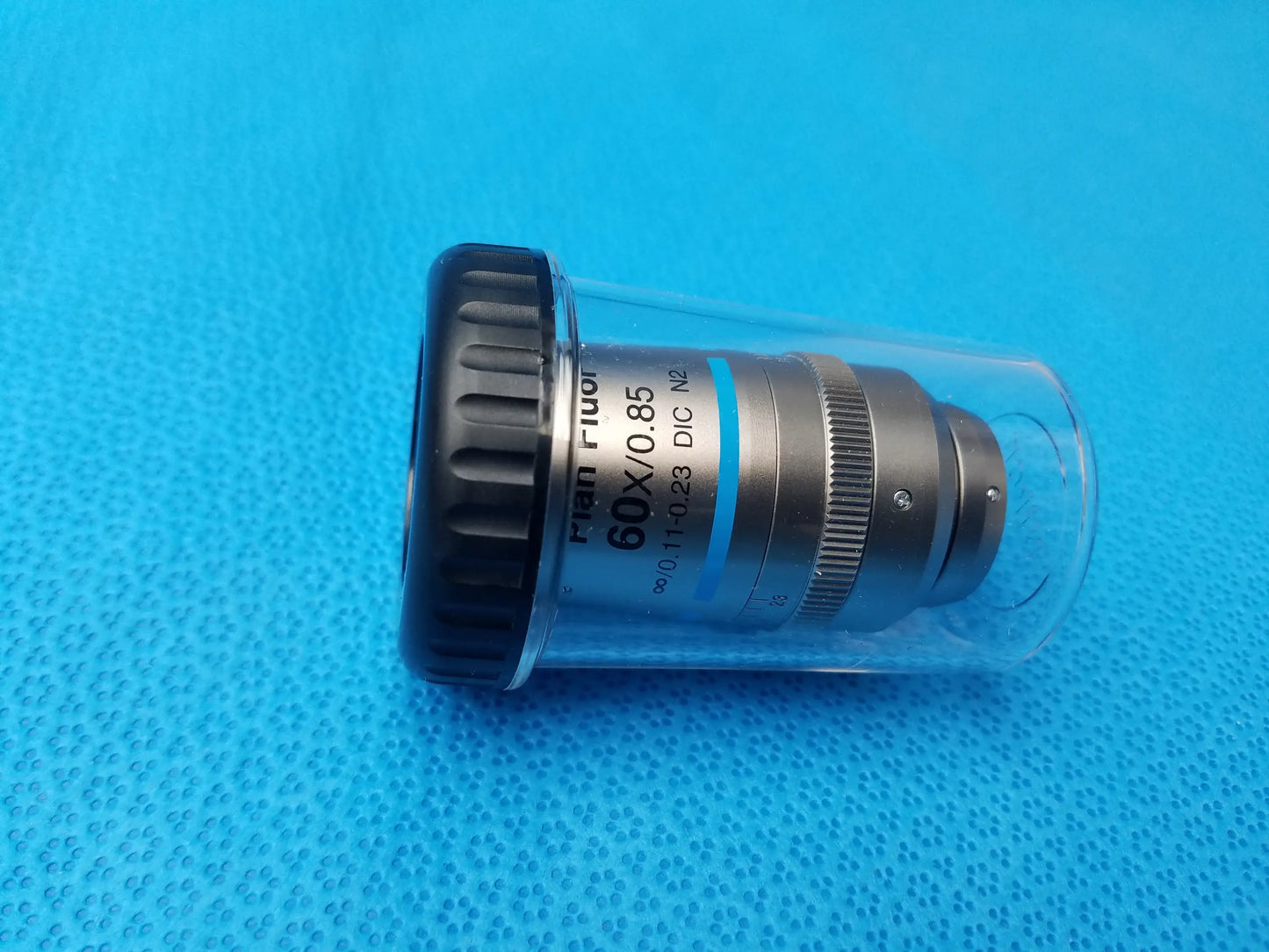 Nikon Plan fluor 60x microscope objective lens with black textured ring and metallic body in clear protective casing compatible Nikon
