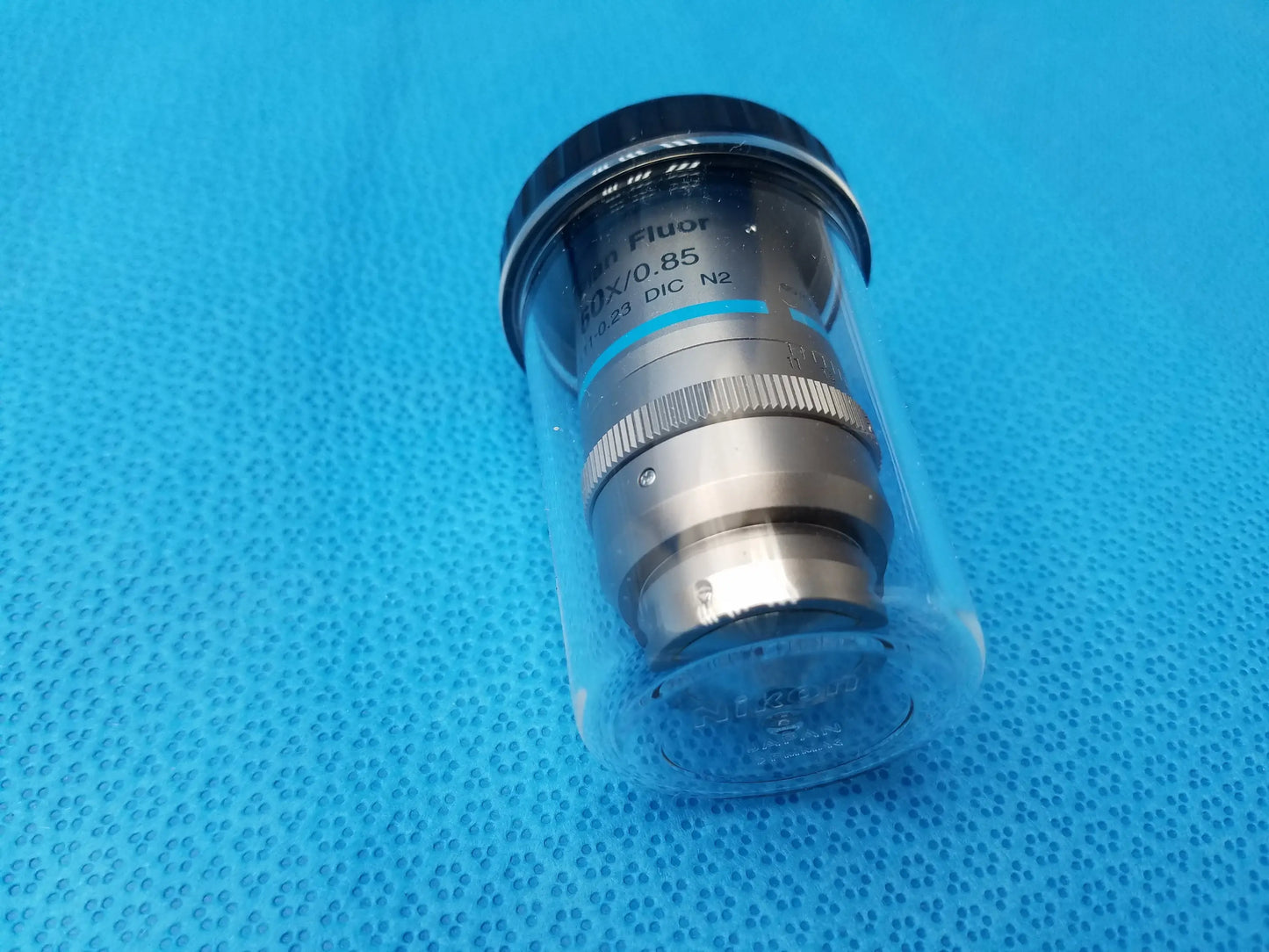 Silver metallic Nikon plan fluor microscope objective with black threaded cap in clear protective casing compatible Nikon