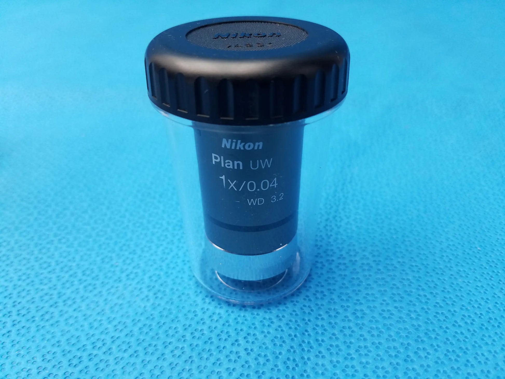 Nikon plan uw 1x 0.04 microscope objective lens with black threaded cap and clear protective casing for compatible nikon microscope systems