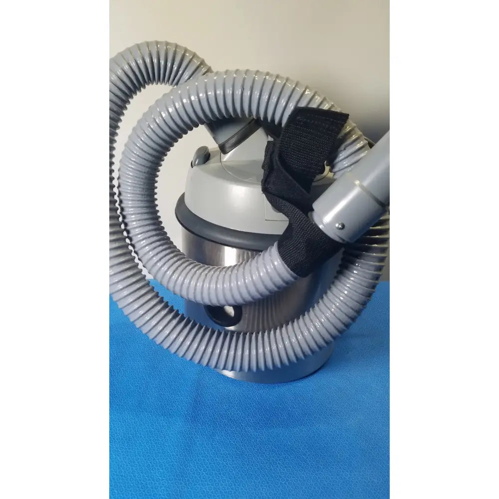Gray corrugated hose with black strap on silver vacuum base of nilfisk advance hovermatt air supply unit