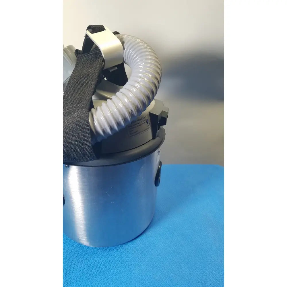 Silver cylindrical nilfisk hovermatt air supply unit with flexible gray corrugated hose and black straps for air purification