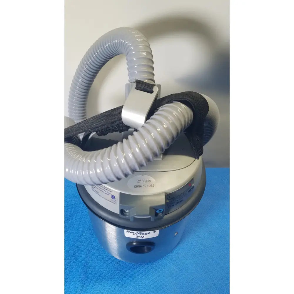 Gray corrugated hose with black strap and metal clamps attached to metallic base of nilfisk hovermatt air supply unit