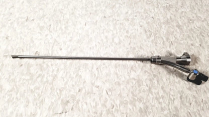 Silver surgical instrument with slender metallic shaft and black handle with blue accents in olympus a20975a endoscope bridge