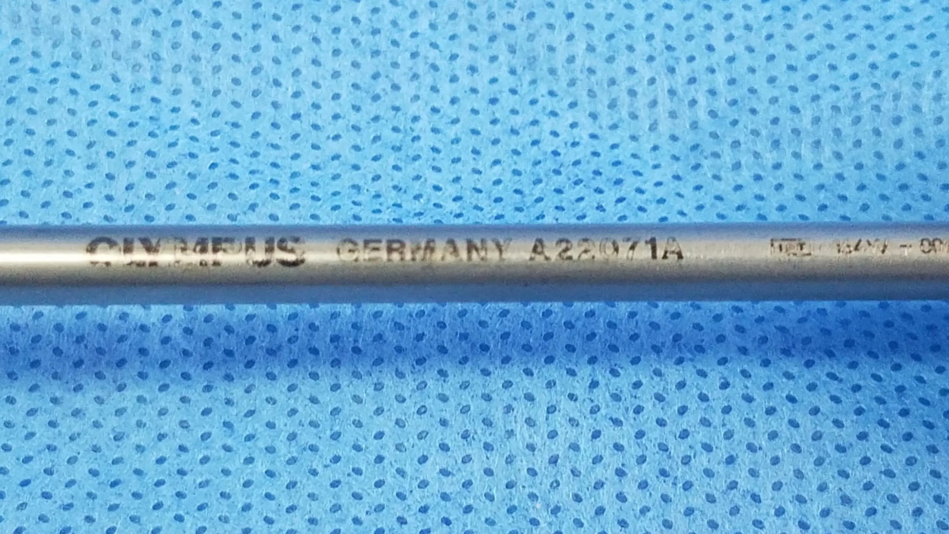 A metallic cylindrical visual optical obturator electrode engraved with oymeus germany a22071a resting on blue surface