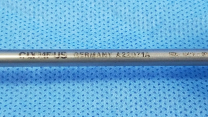 A metallic cylindrical visual optical obturator electrode engraved with oymeus germany a22071a resting on blue surface