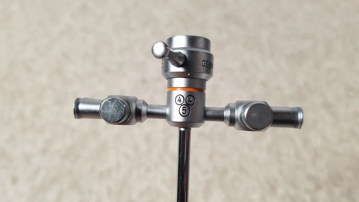 Silver surgical instrument with central shaft and three knotted arms including orange band showing olympus a3723 pediatric sheath