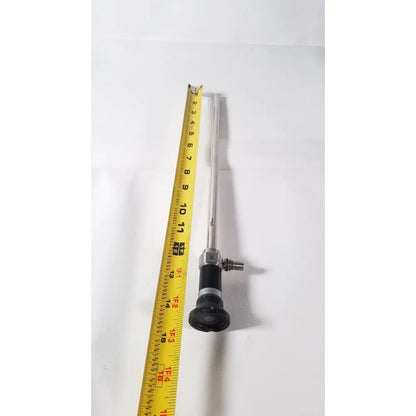 Silver olympus a5254 10mm laparoscope with black handle and metallic joints next to yellow measuring tape