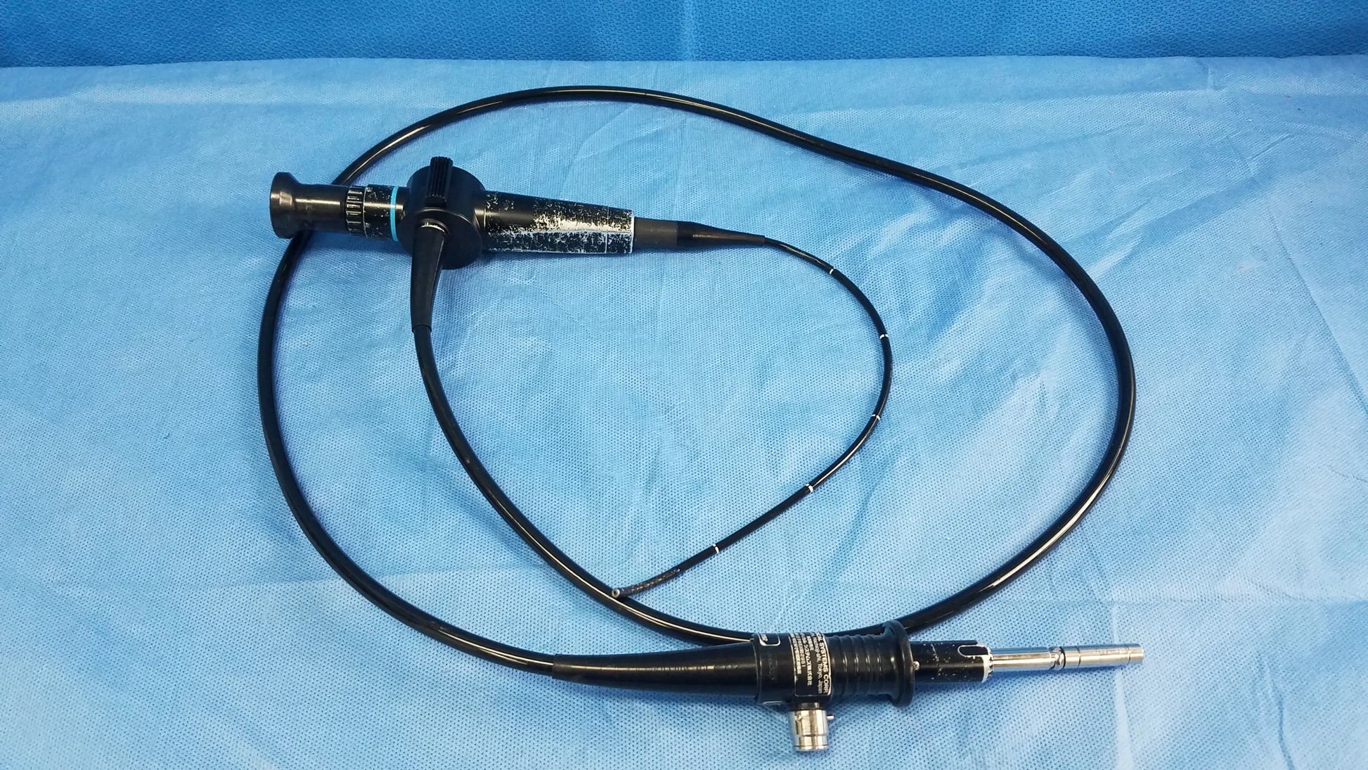 Black flexible fiber optic endoscope olympus enf-p4 rhino-laryngoscope fiberscope coiled on blue surgical drapes