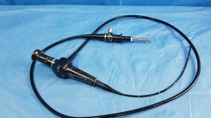 Black Olympus medical systems flexible fiber optic rhino-laryngoscope with textured grip coiled on blue surgical drapes