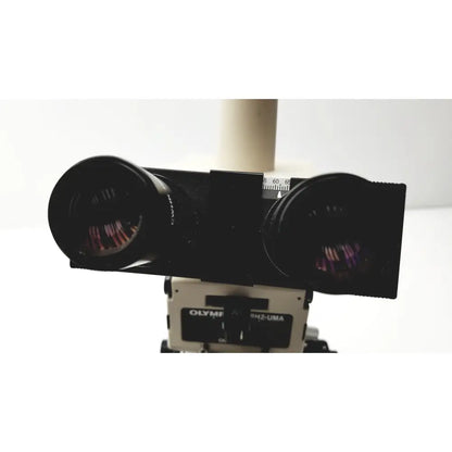 Black dual-lens camera mount with olympus branding on a white base for the olympus optical bh2-uma microscope