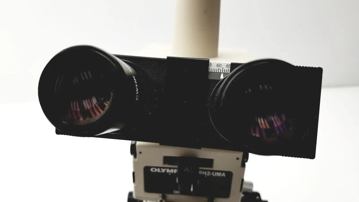 Black dual-lens camera mount with olympus branding on a white base for the olympus optical bh2-uma microscope
