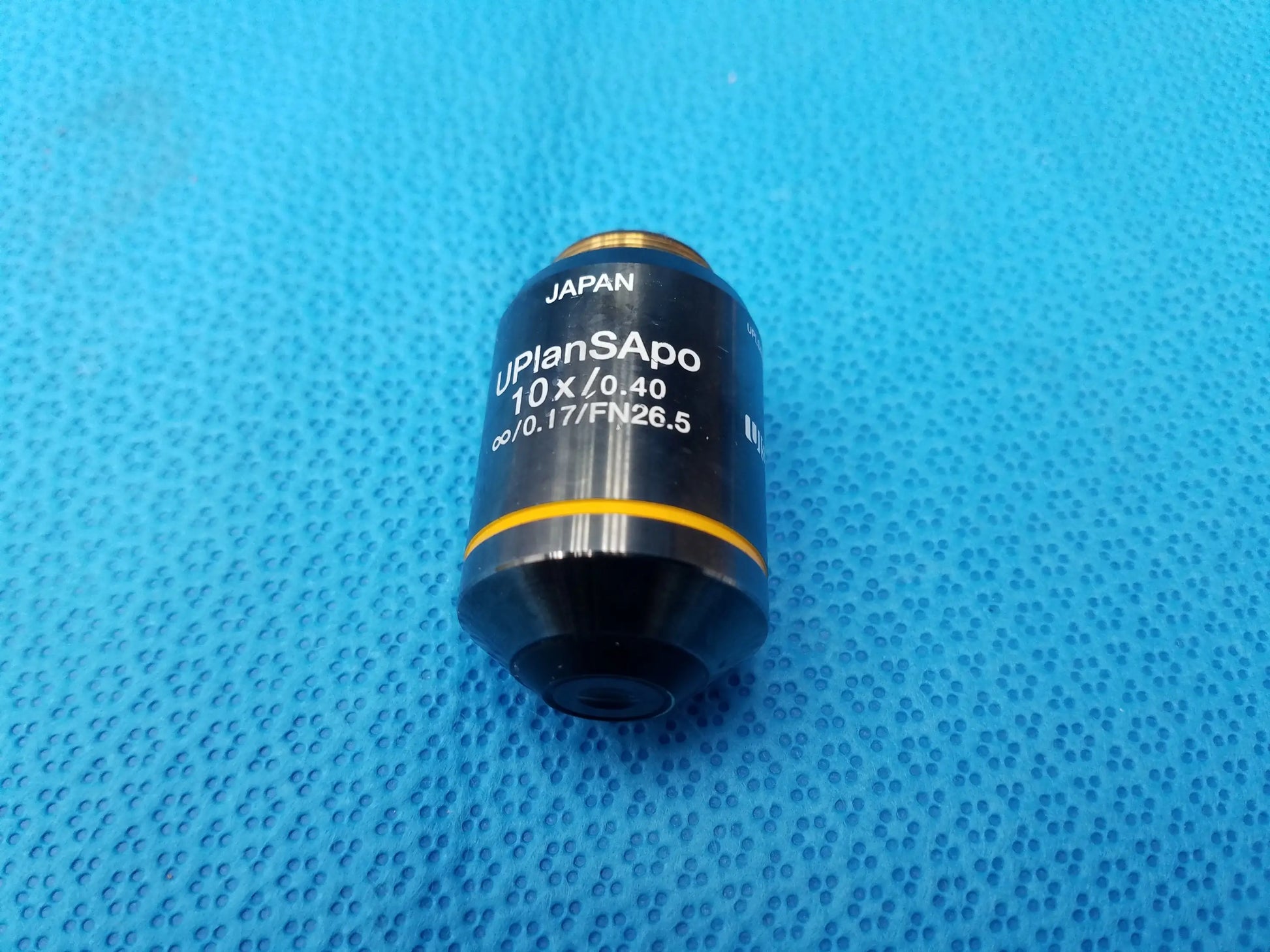 Black and yellow olympus uplansapo 10x microscope objective lens with gold threaded mount marked japan visible on barrel