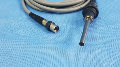 Gray and black Olympus WA03200A S fiber optic light cable with metallic connector coiled on blue surgical drapes