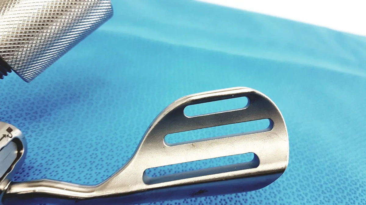 Silver surgical support arm with textured mesh handle and three slots in flat paddle head for stable surgical retraction