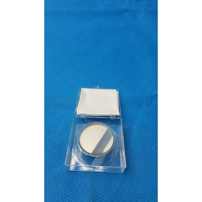 A round off-white optical container compact powder with metallic silver rim and clear plastic case by spawr industries