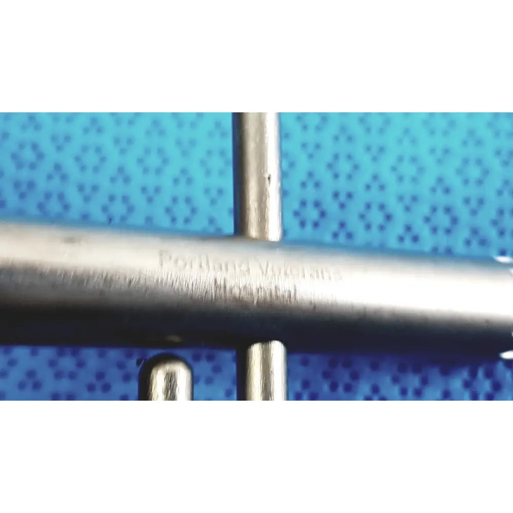 Metallic orthopedic drill chuck key with engraved portland veterans hospital text and cross-shaped metal frame behind it
