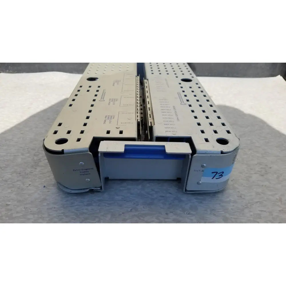 Silver metallic surgical instrument tray with blue plastic latch and perforated sides for pelvic fragment reuse medical use