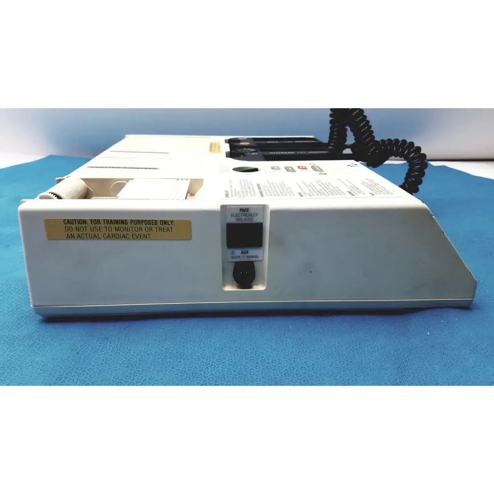 White plastic physio control lifepak 10 cardiac monitor with black coiled cable and yellow warning label visible