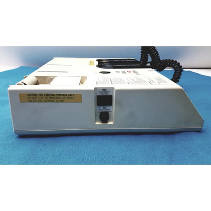 White plastic physio control lifepak 10 cardiac monitor with black coiled cable and yellow warning label visible