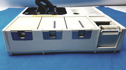 White and blue physio control lifepak 10 cardiac monitor with three labeled compartments and open paper roll compartment