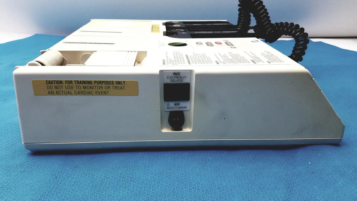 White plastic physio control lifepak 10 cardiac monitor with black coiled cable and yellow warning label visible