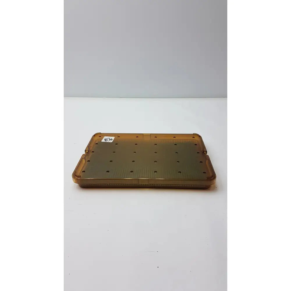 Transparent amber plastic sterilization tray with grid of circular holes and silicone finger mat for plastic sterilization