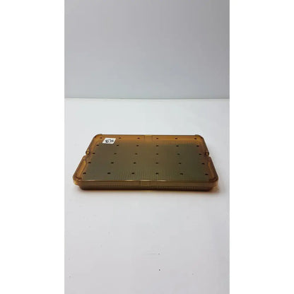 Transparent amber plastic sterilization tray with grid of circular holes and silicone finger mat for plastic sterilization