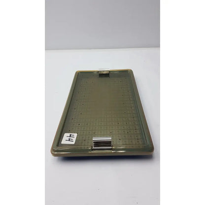 Olive-green plastic sterilization tray with metallic clasp and perforated surface featuring silicone finger mat