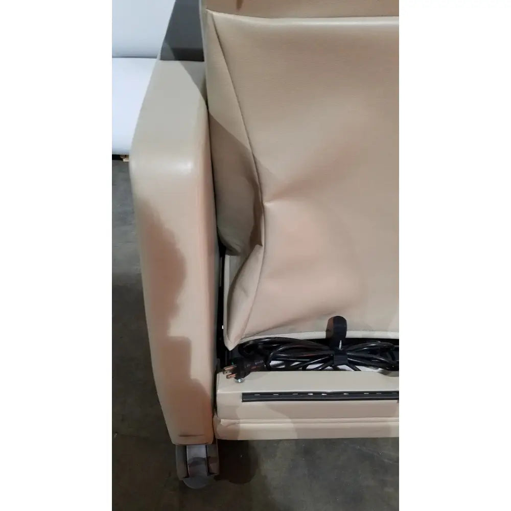 Beige upholstered power recovery recliner armrest with hand control power cord and caster wheel visible