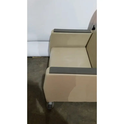 Beige upholstered power recovery recliner with dark gray armrests and casters featuring hand control