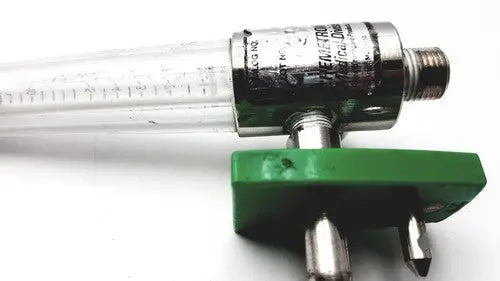 Clear glass tube with metallic threaded end and green connector for a precision medical regulator gauge
