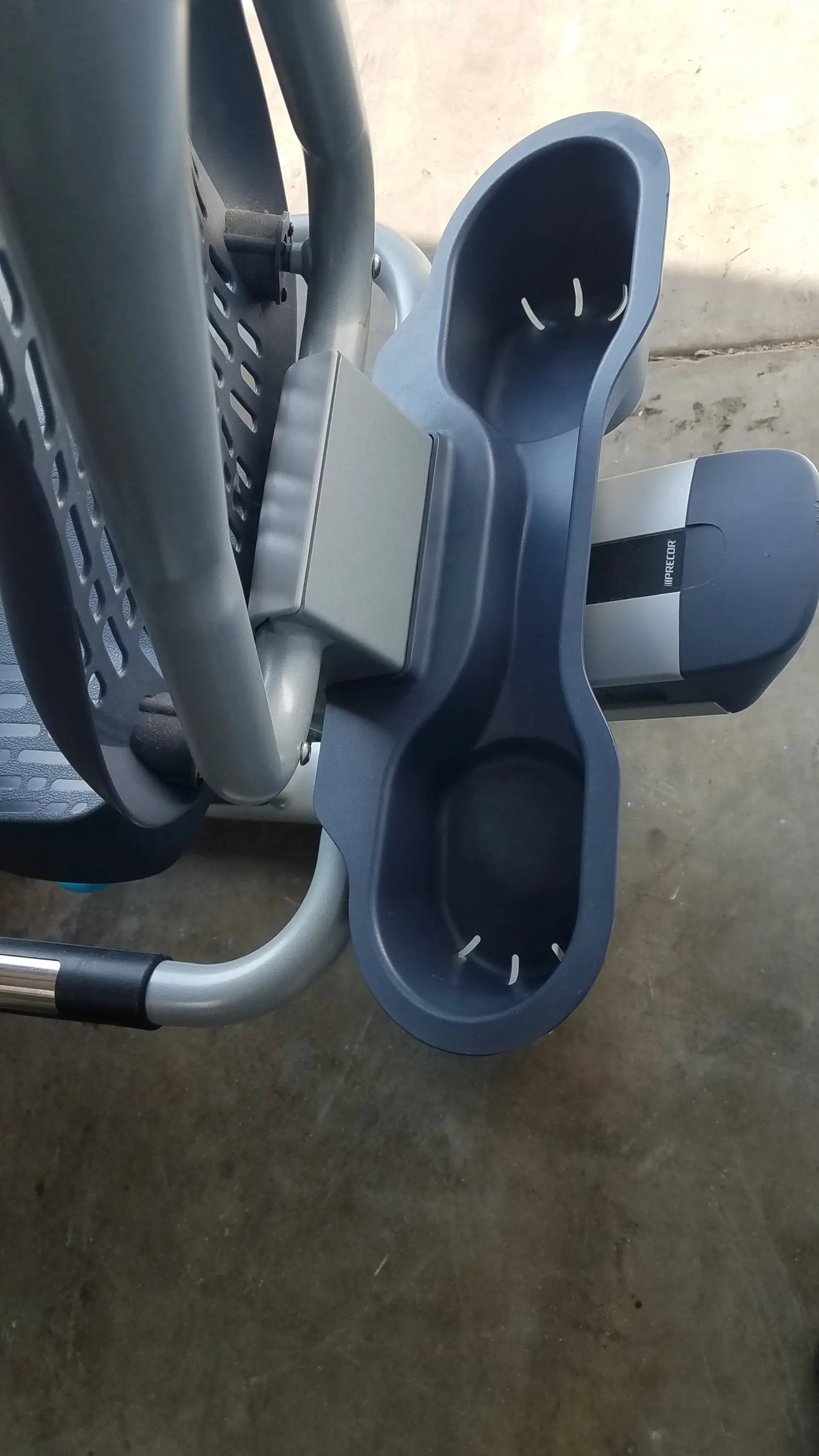 Dark gray plastic cup holder with two compartments and white stitching on precor recumbent exercise bike with precor console