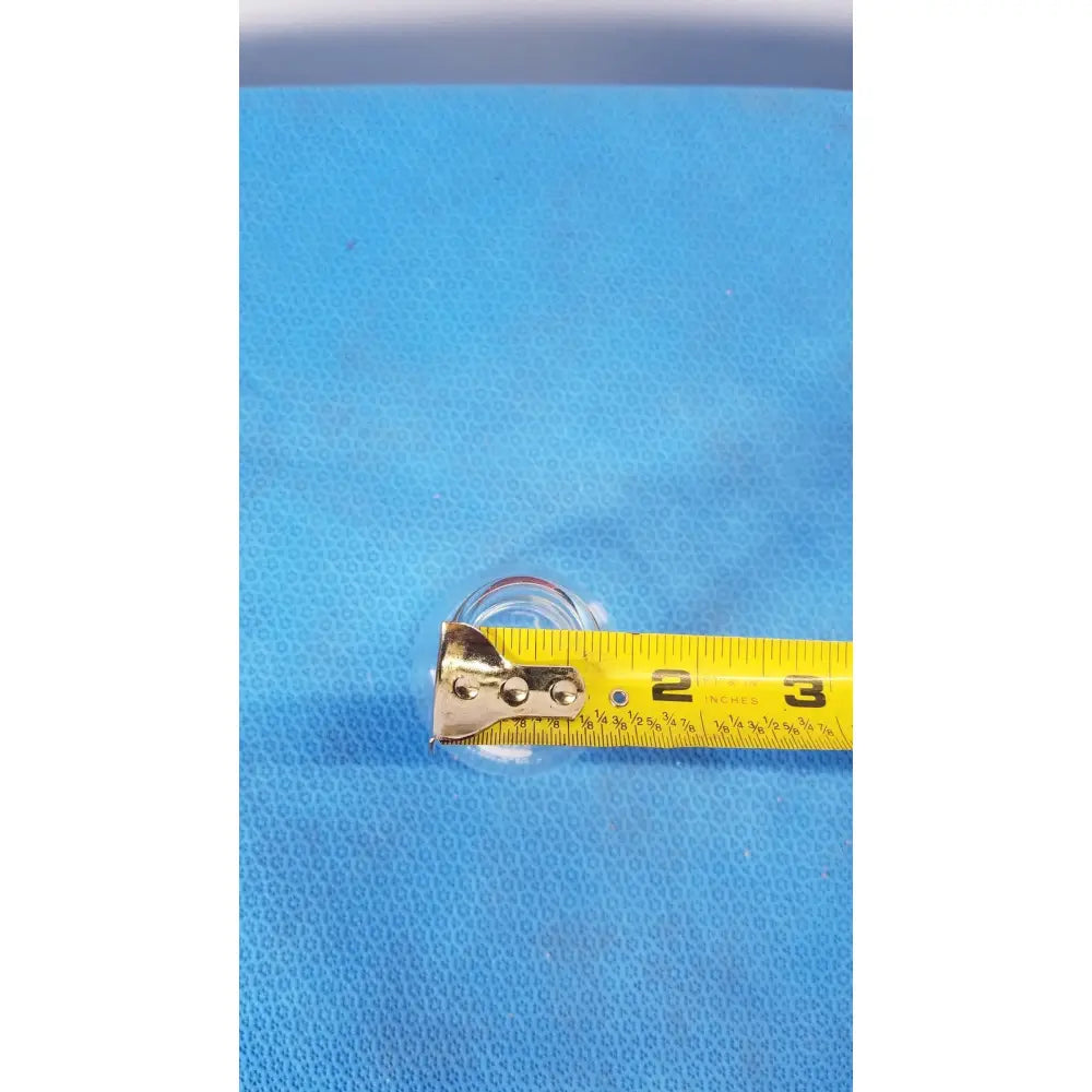 A yellow measuring tape with metallic silver casing lies horizontally beside a pyrex 125 ml glass erlenmeyer conical flask heavy duty rim