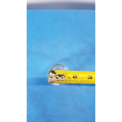 A yellow measuring tape with metallic silver casing lies horizontally beside a pyrex 125 ml glass erlenmeyer conical flask heavy duty rim