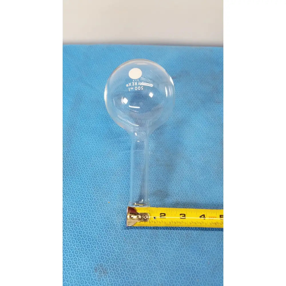 Clear glass pyrex 500ml single neck round bottom boiling flask marked 500 ml on a blue surface with a yellow tape