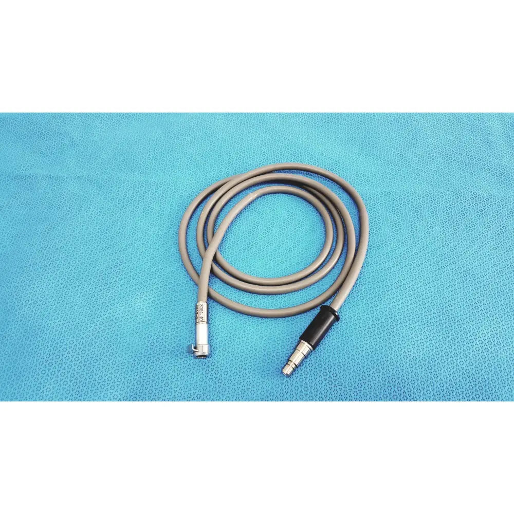Gray medical-grade fiberoptic light cable with metallic connectors coiled on blue surface for surgical illumination