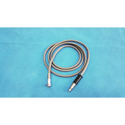 Gray medical-grade fiberoptic light cable with metallic connectors coiled on blue surface for surgical illumination