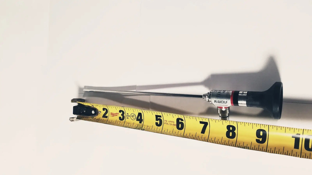 A black and silver r-wolf 8880.433 panoview 25 degree rigid arthroscope with a slender metallic shaft beside a yellow measuring tape