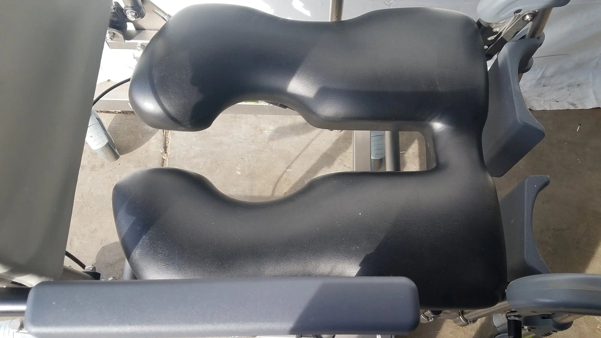 Black padded seat with contoured ergonomic support on raz attendant tilt shower commode chair for medical use