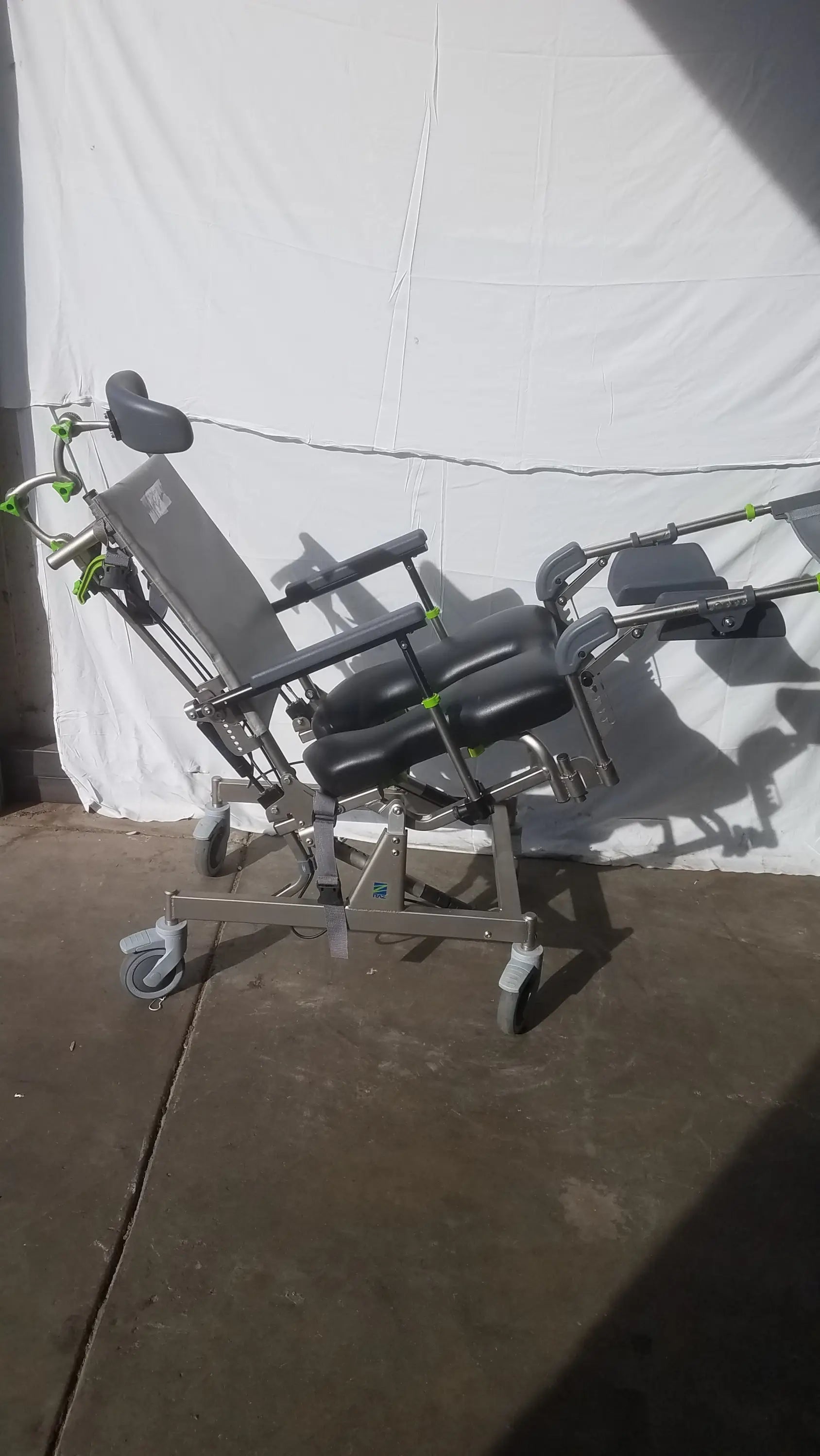 Gray adjustable raz attendant tilt shower commode chair with black padded sections and green accent hardware on wheels