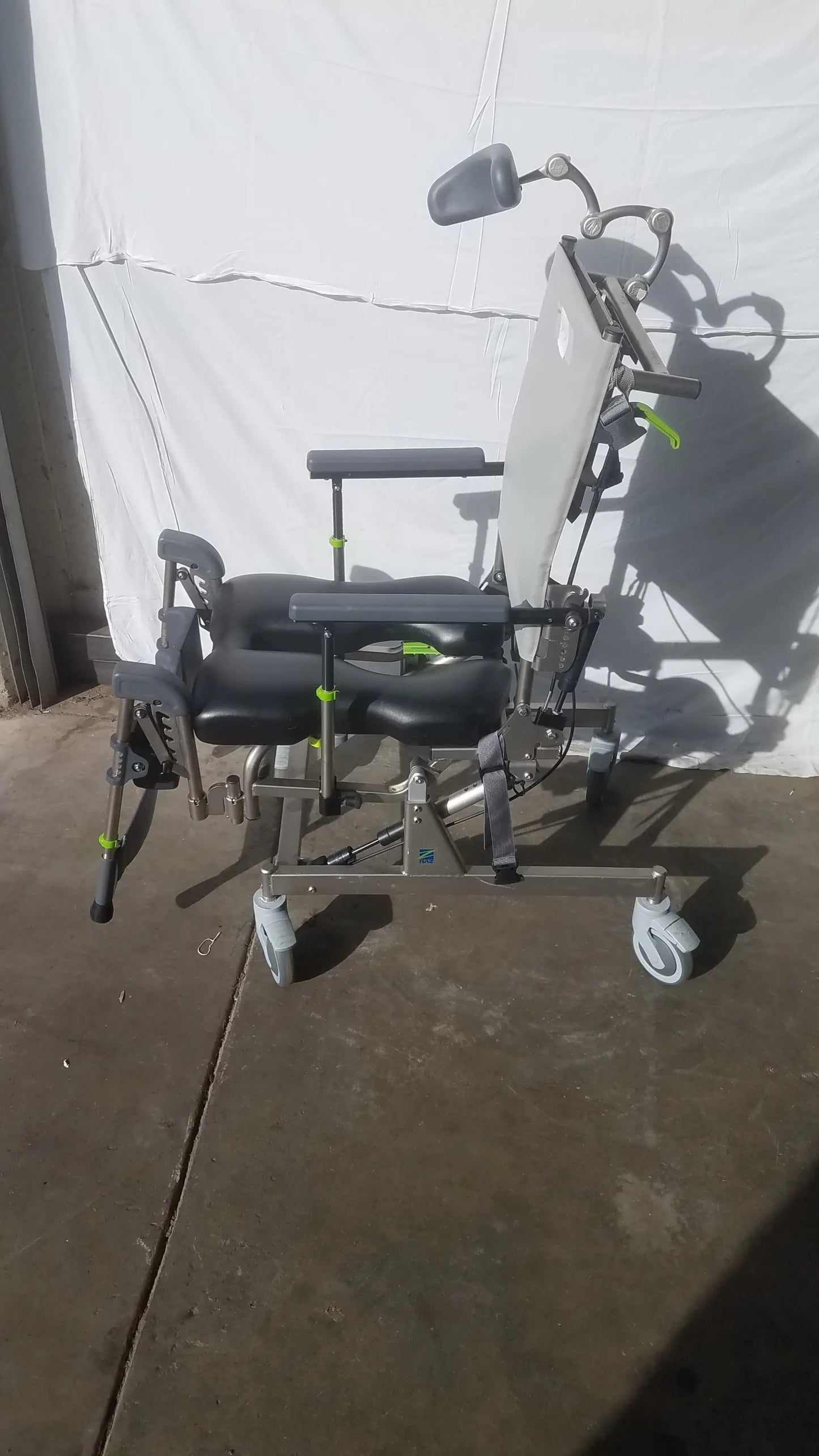 Gray and black adjustable Raz Attendant tilt shower commode chair with wheels, headrest support, and padded seating