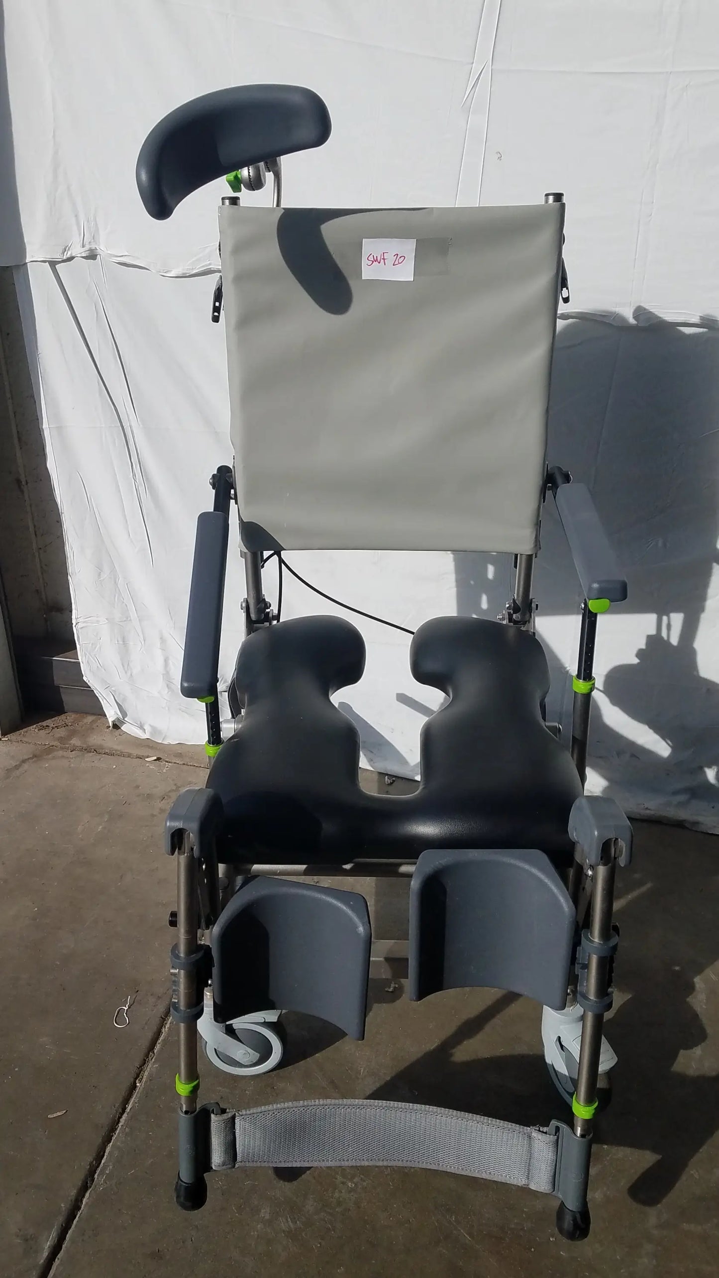 Gray and black adjustable Raz attendant tilt shower commode chair with padded headrest armrests and foot supports