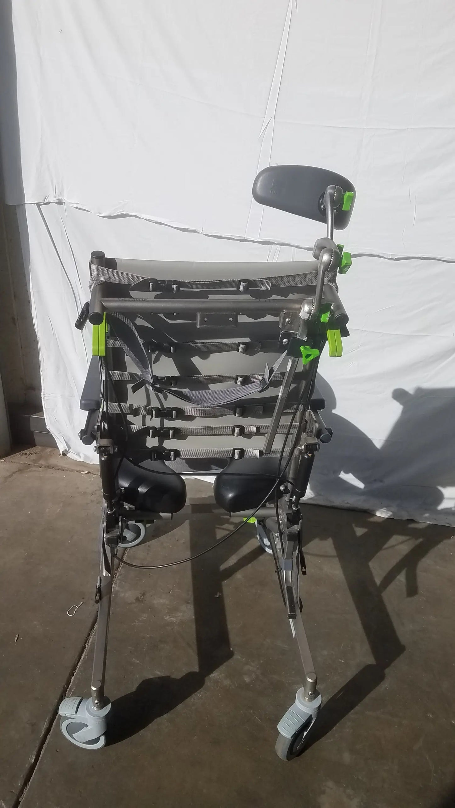 Gray and black Raz attendant tilt shower commode chair with adjustable armrests, padded seat, and four caster wheels