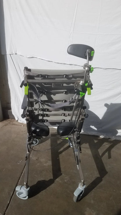 Gray and black Raz attendant tilt shower commode chair with adjustable armrests, padded seat, and four caster wheels