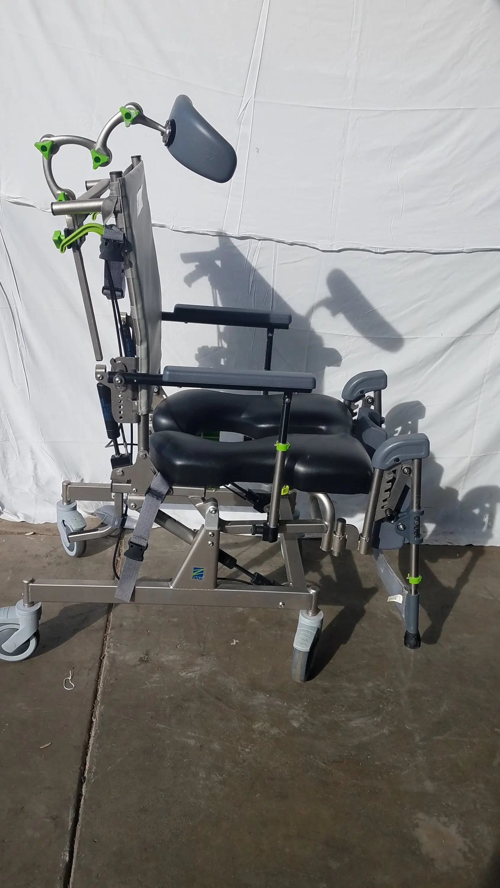 Gray and green Raz Attendant tilt shower commode chair with padded black seat, metal frame, and caster wheels
