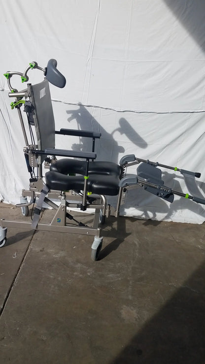 Raz attendant tilt shower commode chair with silver metal frame, black padded cushions, green accents, adjustable headrest and leg supports