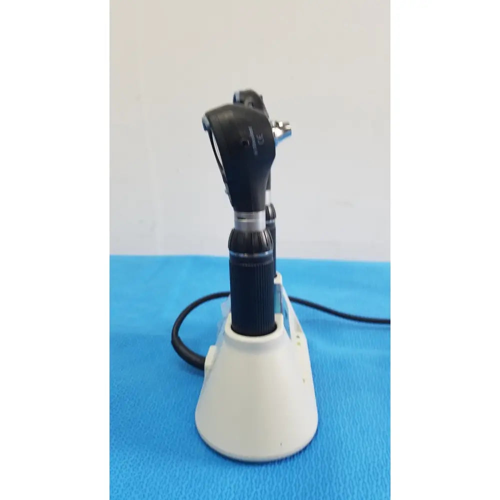 Black and silver medical otoscope with textured grip resting on white riester ri-charger l charging base stand