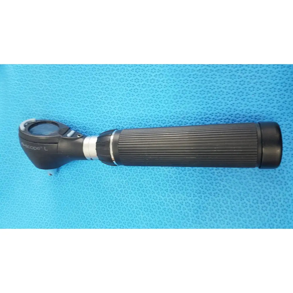 Black ribbed-handled ophthalmoscope with circular lens and silver accents shown with riester ri-charger l charging base