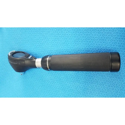 Black ribbed-handled ophthalmoscope with circular lens and silver accents shown with riester ri-charger l charging base