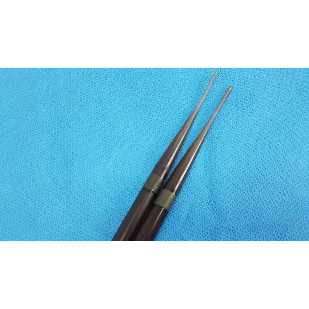 A pair of dark brown polished wooden drumsticks with silver bands shown alongside savary gilliard dilator cook endoscope 19mm